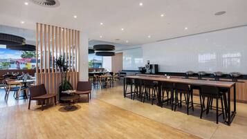 Un restaurante moderno con suelo de madera, una barra larga con taburetes y una pantalla grande que muestra un paisaje urbano.