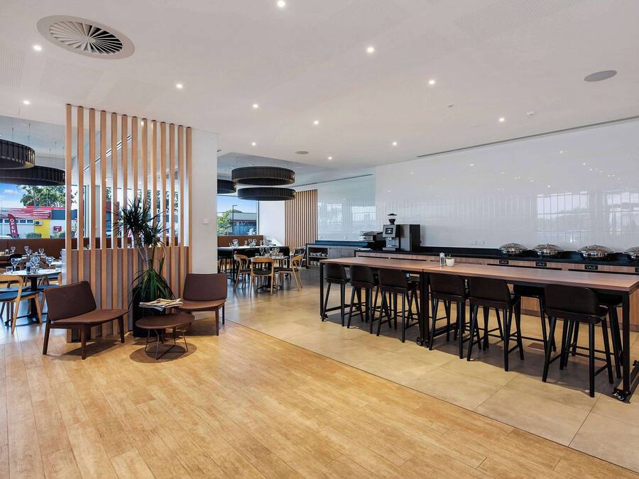 Un restaurante moderno con suelo de madera, una barra larga con taburetes y una pantalla grande que muestra un paisaje urbano.