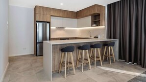 Una cocina moderna con una isla central, taburetes de bar y un refrigerador de acero inoxidable.