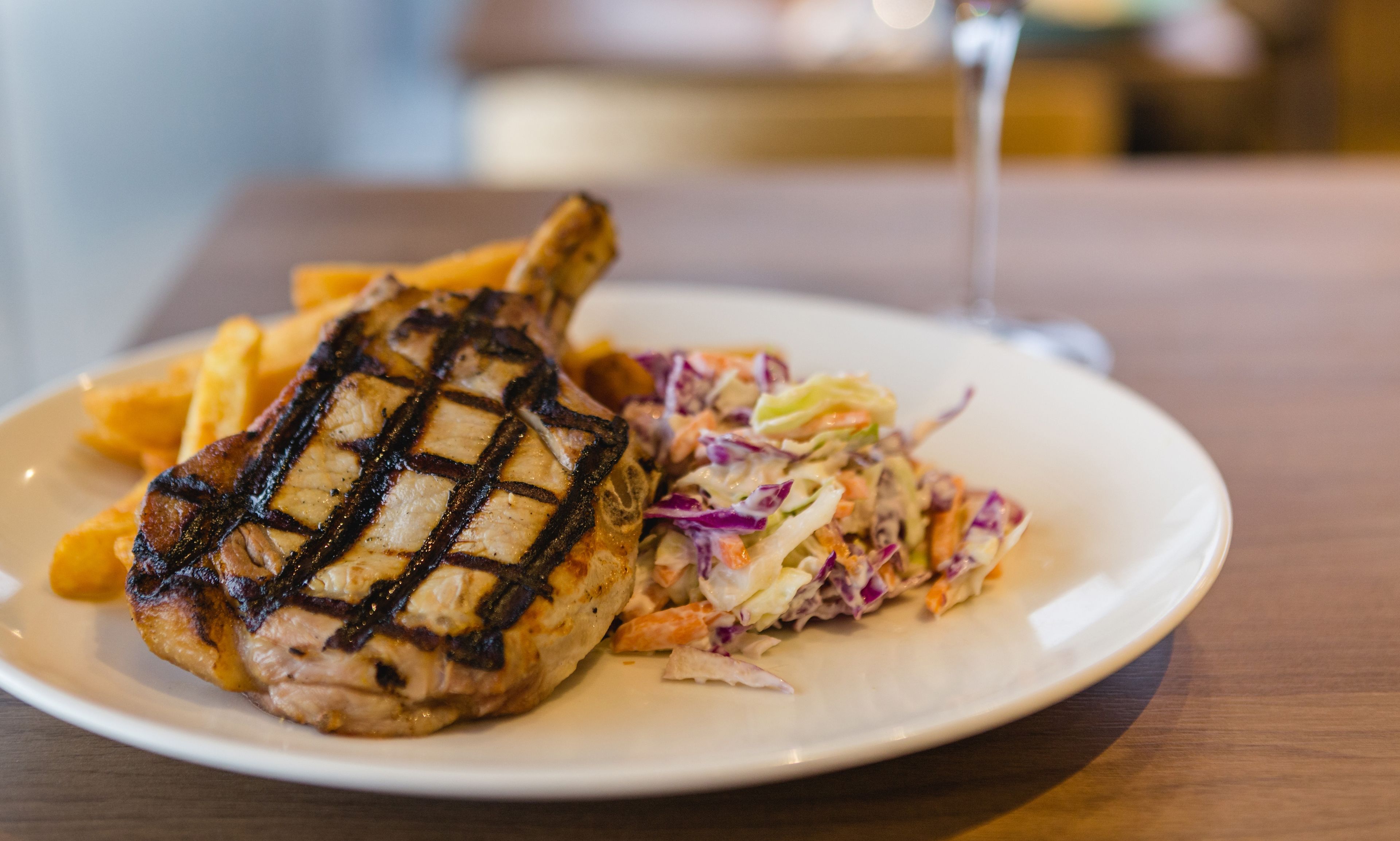 A plate with grilled chicken and coleslaw on a wooden table.