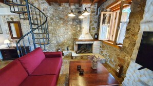 A cozy living area with a red sofa, a wooden coffee table, a stone fireplace, and a spiral staircase. - Villa Kalata (Lefkada)