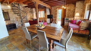 A rustic interior with a stone wall, wooden ceiling beams, a dining table with chairs, a sofa, and a television. - Villa Kalata (Lefkada)