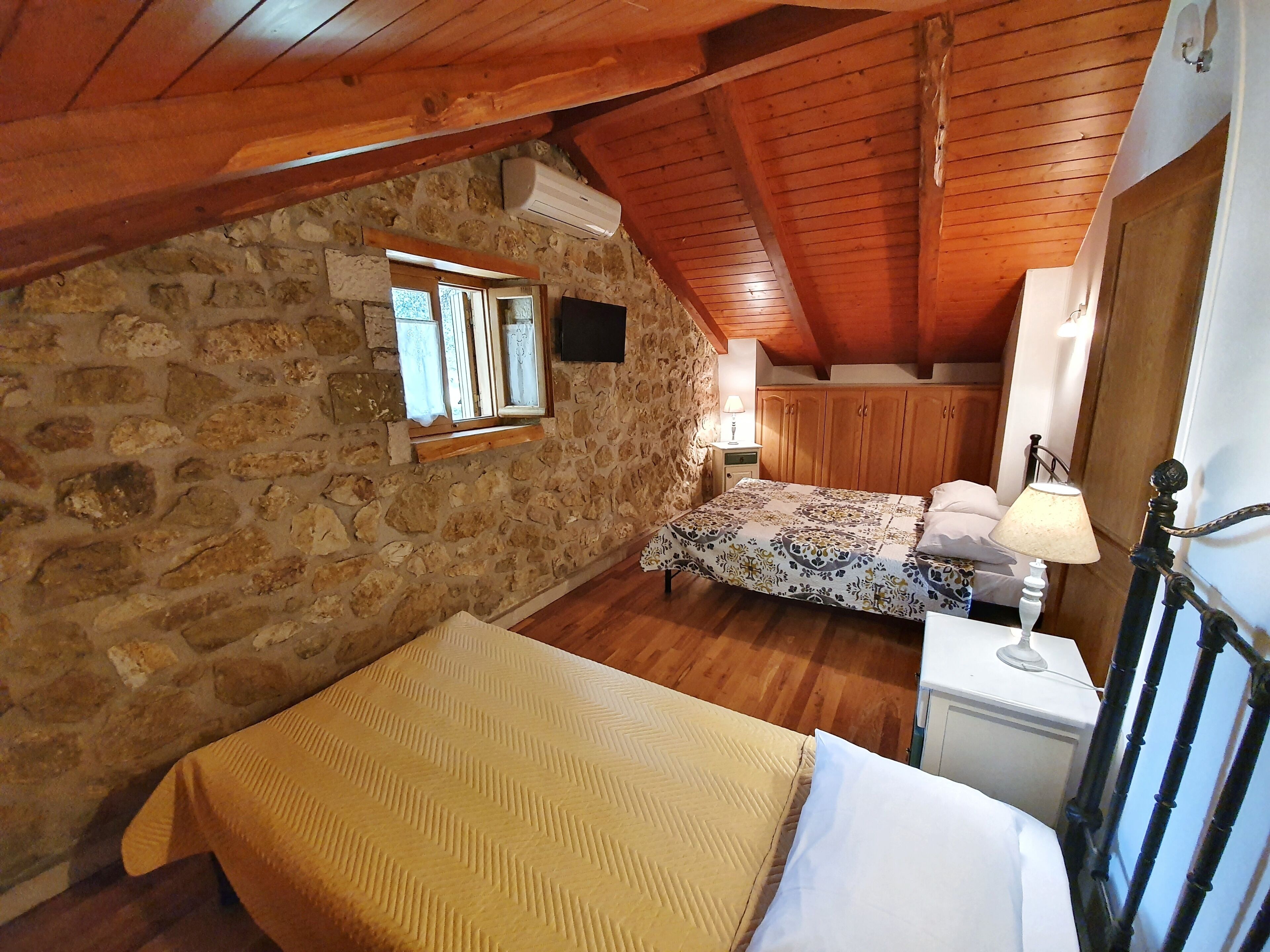 Una habitación acogedora con cama, un armario de madera, pared de piedra y ventana con cortinas.