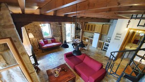 A spacious living area with a red sofa, wooden coffee table, stone flooring, and a kitchen in the background. - Villa Kalata (Lefkada)