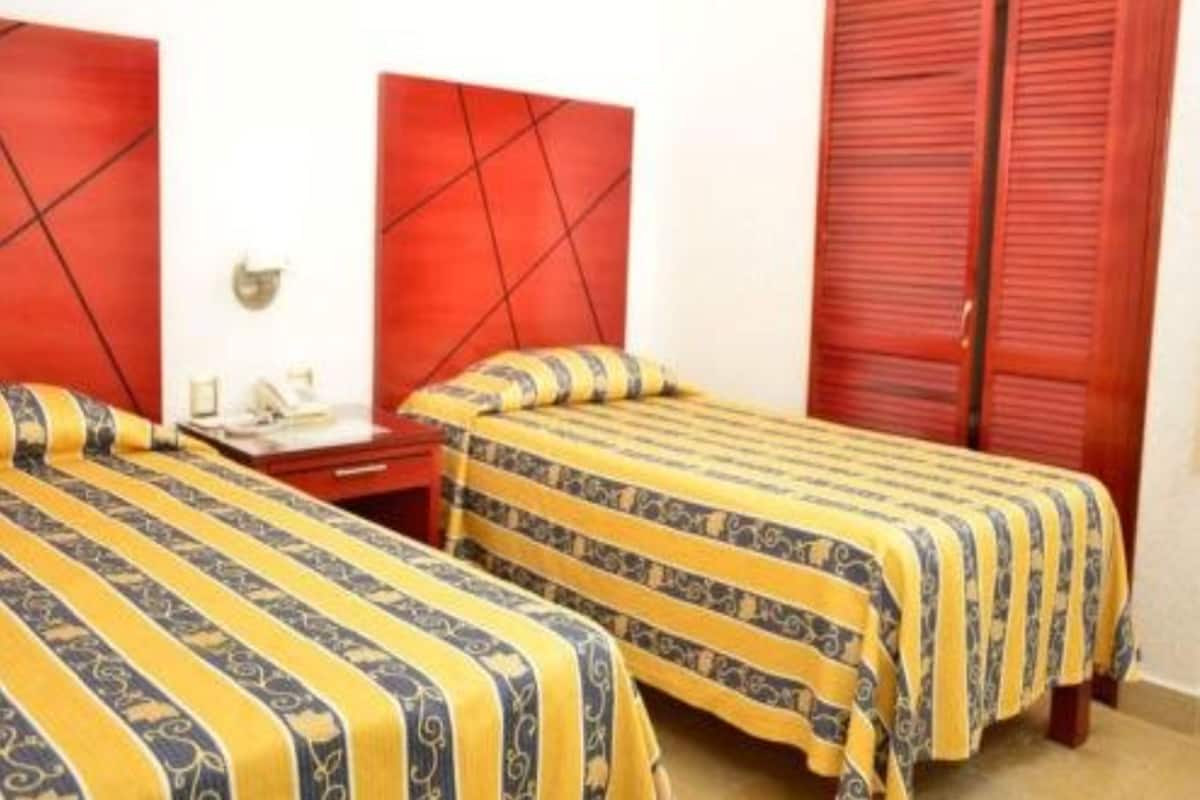 A hotel room with two beds, each with a striped bedspread, a red headboard, and a wooden nightstand with a lamp.