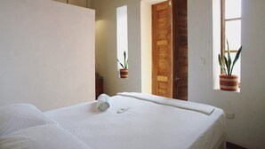 A hotel room with a large bed, a wooden door, and two windows with potted plants. - Tunido - Hostel (Santa Marta)
