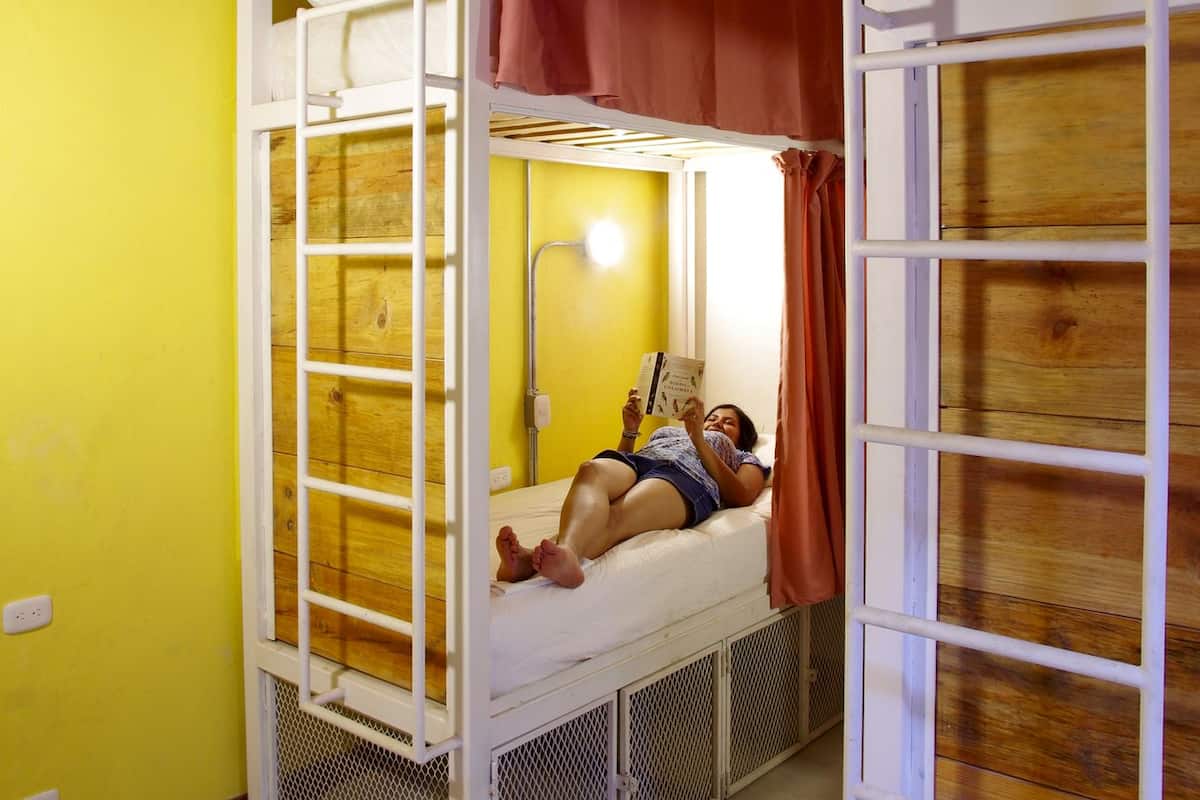 A bunk bed room with a yellow wall, a red curtain, and a single bed with a reading lamp.