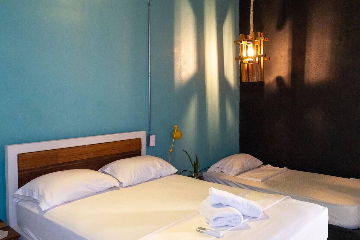 A hotel room with two beds, a wooden headboard, a bedside table, a lamp, and a potted plant.