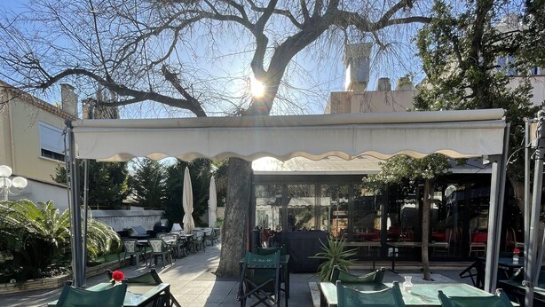 An outdoor patio with green folding chairs and tables, a covered seating area, and a large tree providing shade. - Hotel Les Cigalons (Marseille)