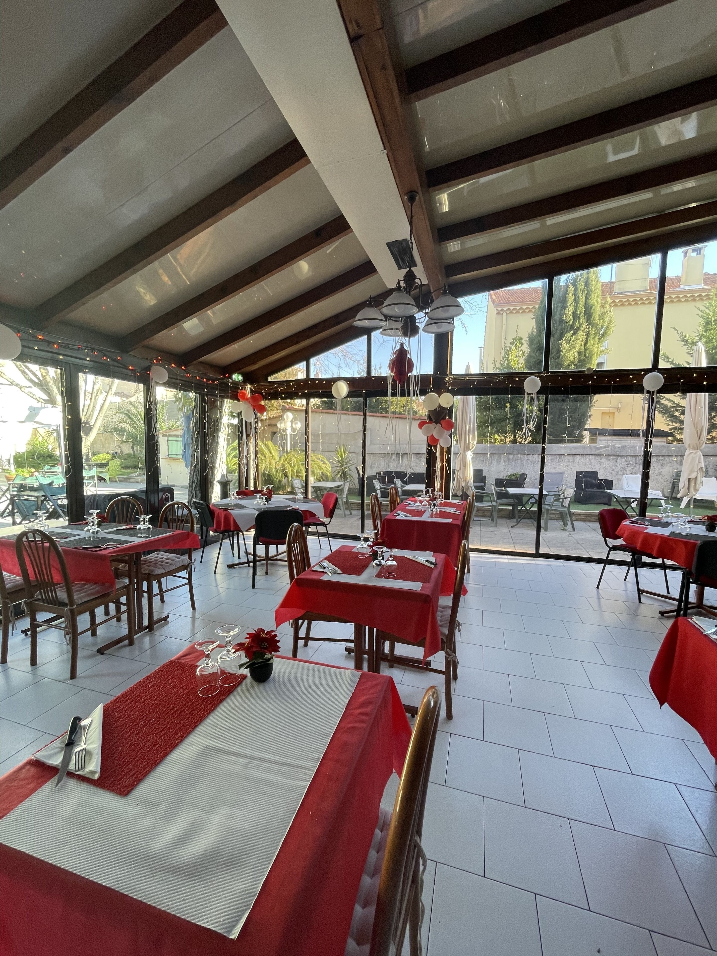 Een restaurant met gedekte tafels, uitgevoerd in rood en wit, met uitzicht op de omgeving.