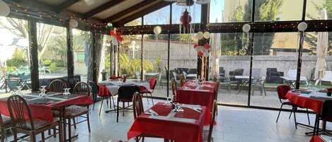 Een restaurant met gedekte tafels, uitgevoerd in rood en wit, met uitzicht op de omgeving.