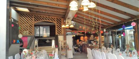 Ein Restaurant mit Holzbalken, weißen Tischdecken und einem langen Essbereich.