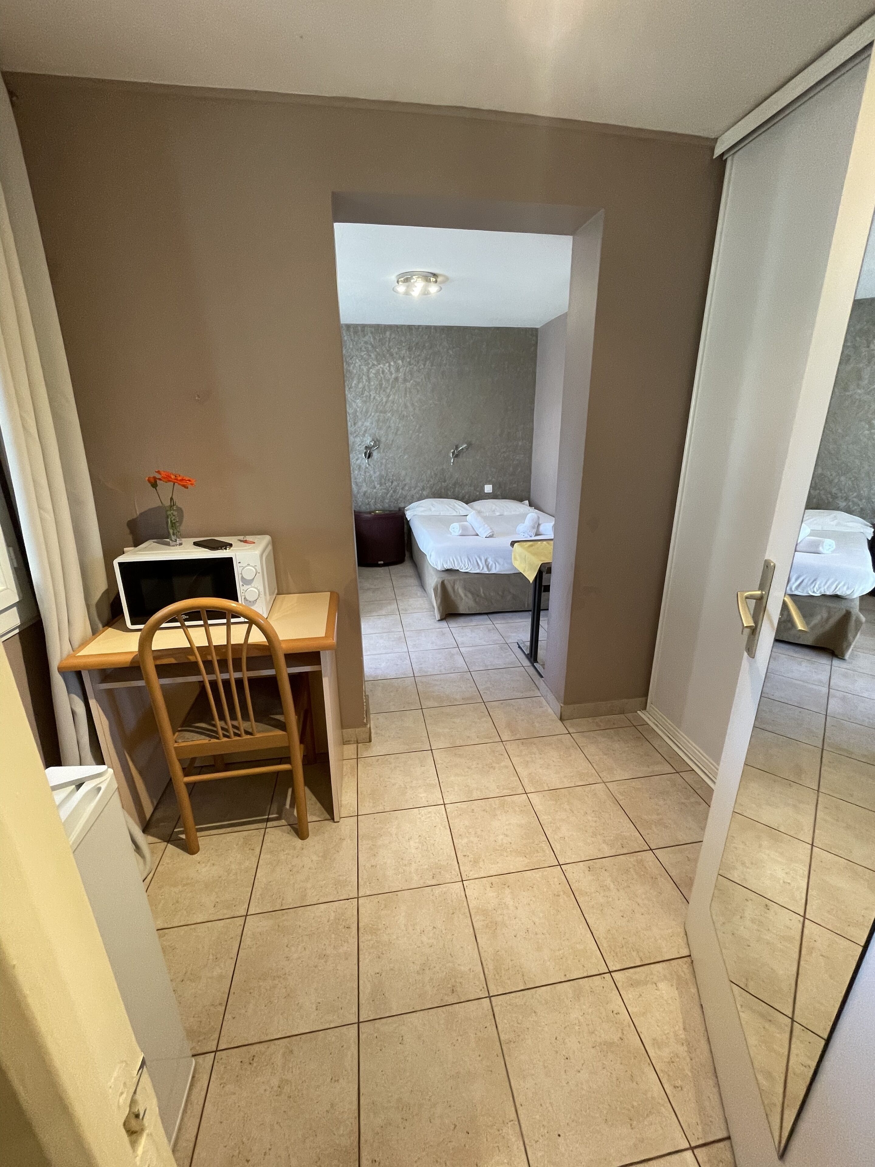 A compact hotel room with a kitchenette, a bed, and a bathroom visible through an open door.