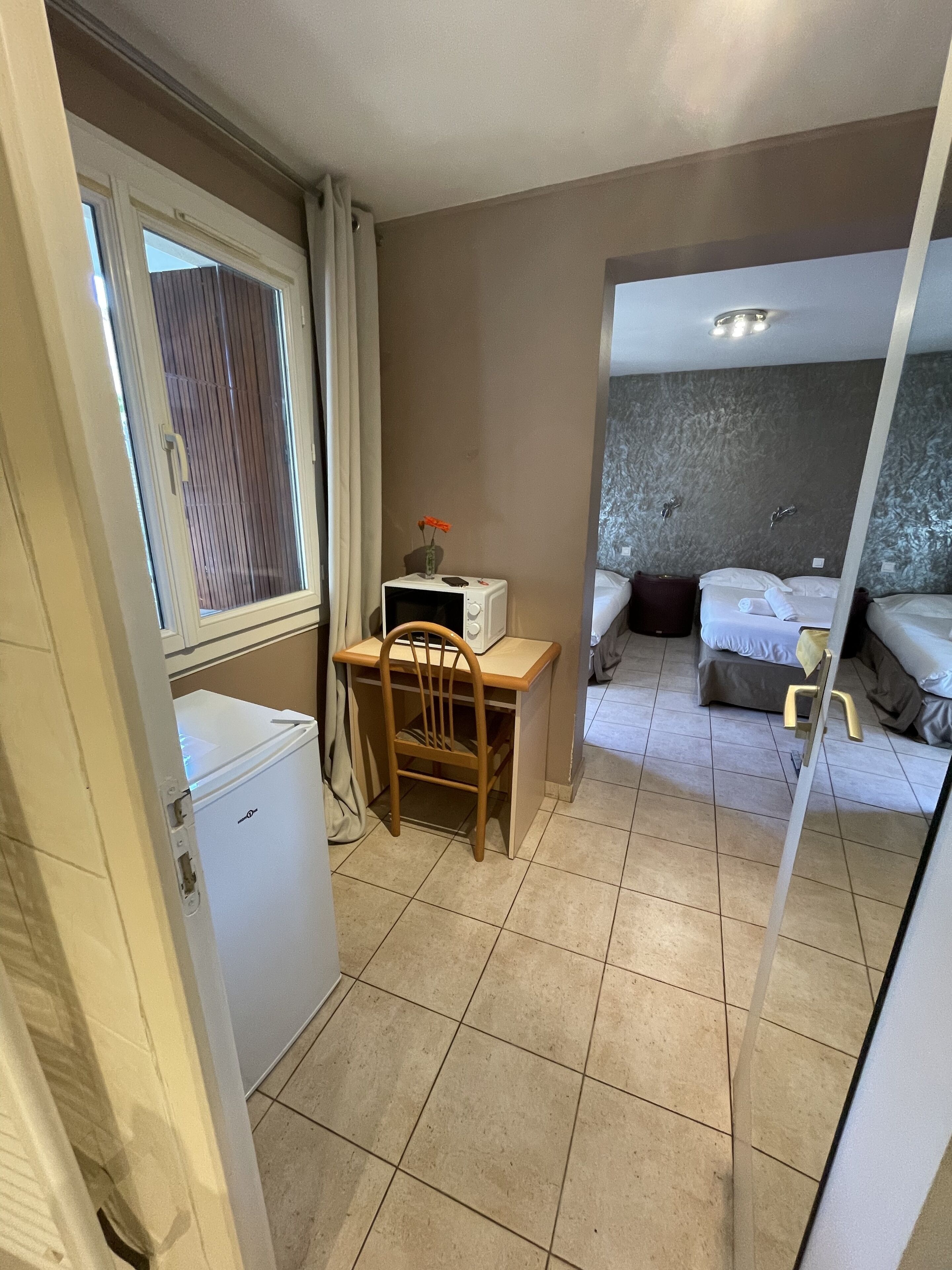 A compact hotel room with a small desk, a chair, a bed, and a bathroom visible through a mirror.