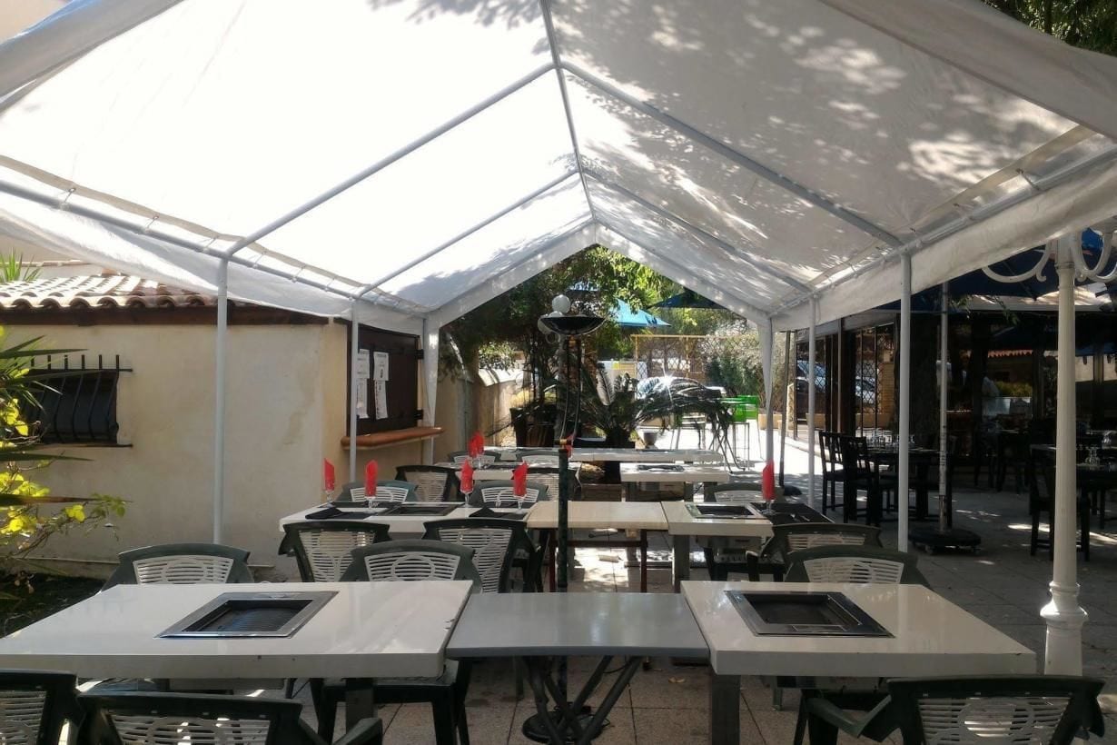 An outdoor dining area with tables and chairs under a large white canopy.