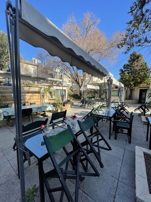 An outdoor patio area with tables and chairs, a covered seating area, and a view of buildings in the background. - Hotel Les Cigalons (Marseille)