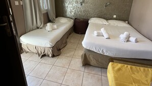 A hotel room with two beds, a small table, a chair, and a window with curtains. - Hotel Les Cigalons (Marseille)