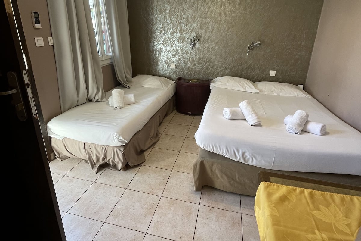 Une chambre d’hôtel avec deux lits, une petite table, une chaise et une fenêtre avec des rideaux.