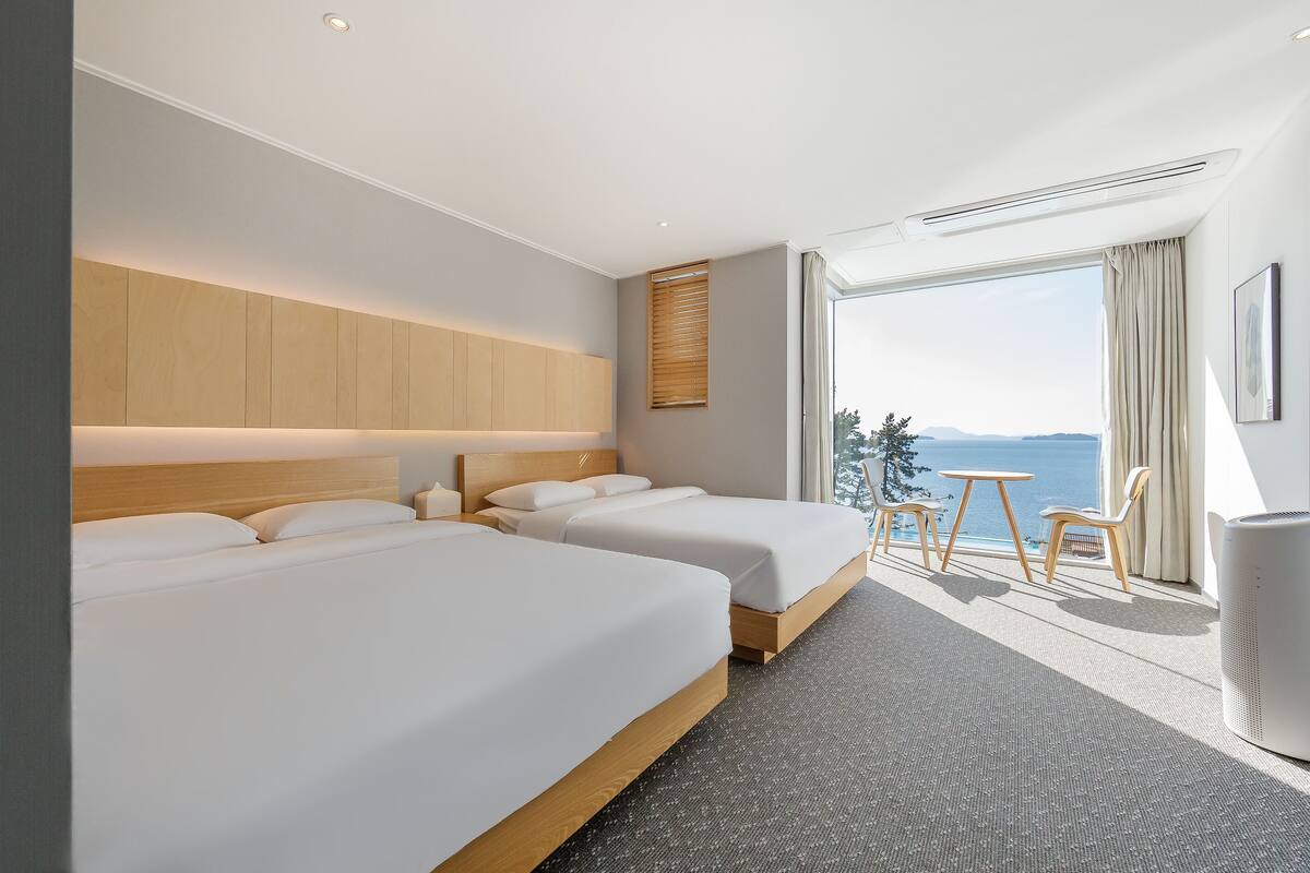 Ein Hotelzimmer mit zwei Betten, einem großen Fenster mit Blick, einem kleinen Tisch und einem Stuhl.