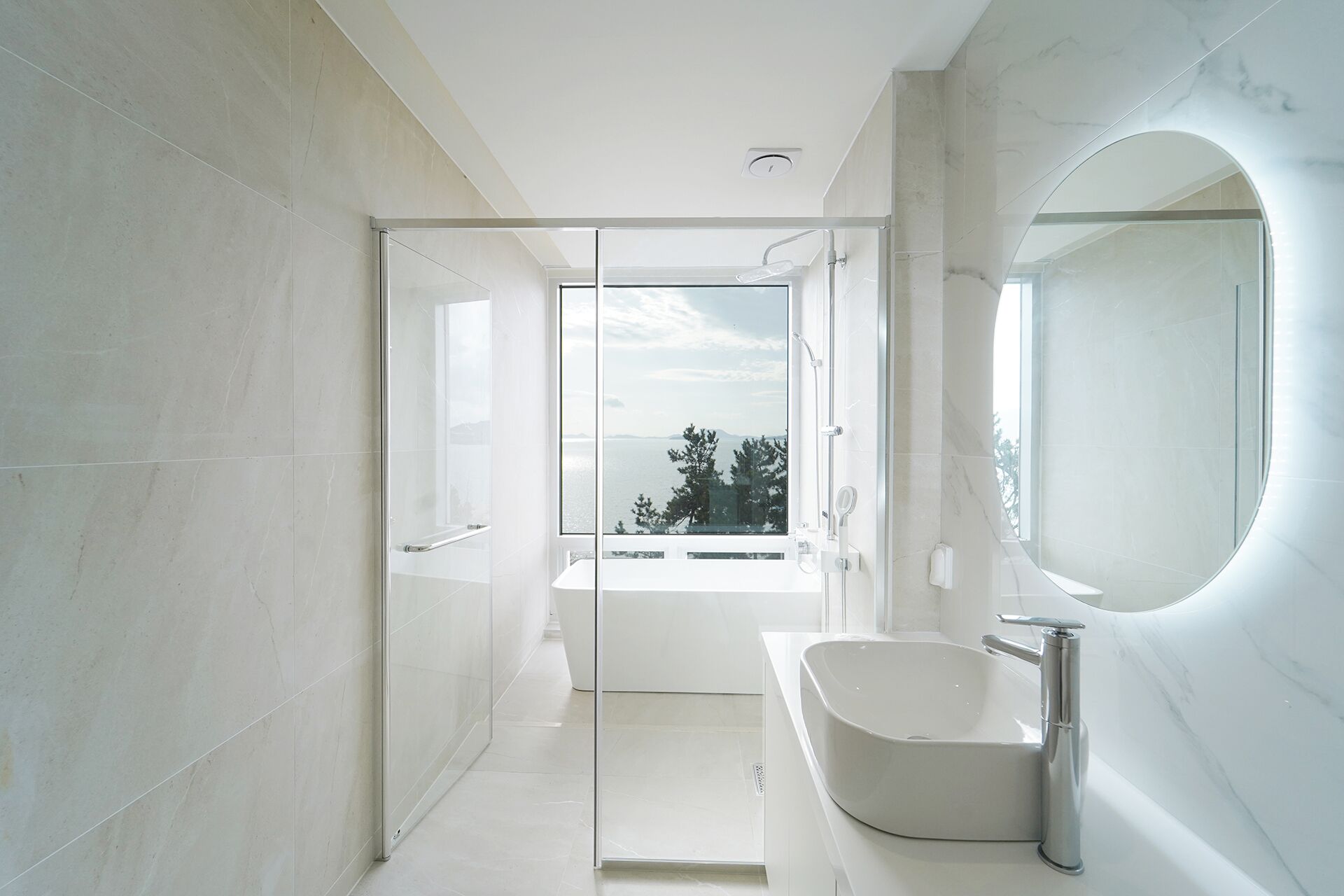 Une salle de bain moderne avec un grand miroir, une baignoire et une vue sur l’extérieur.