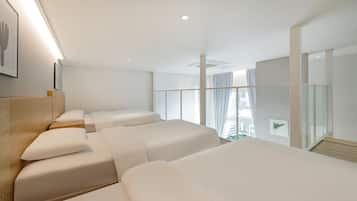 Una habitación de hotel moderna con tres camas, un ventanal grande con vista a la ciudad y un diseño minimalista.