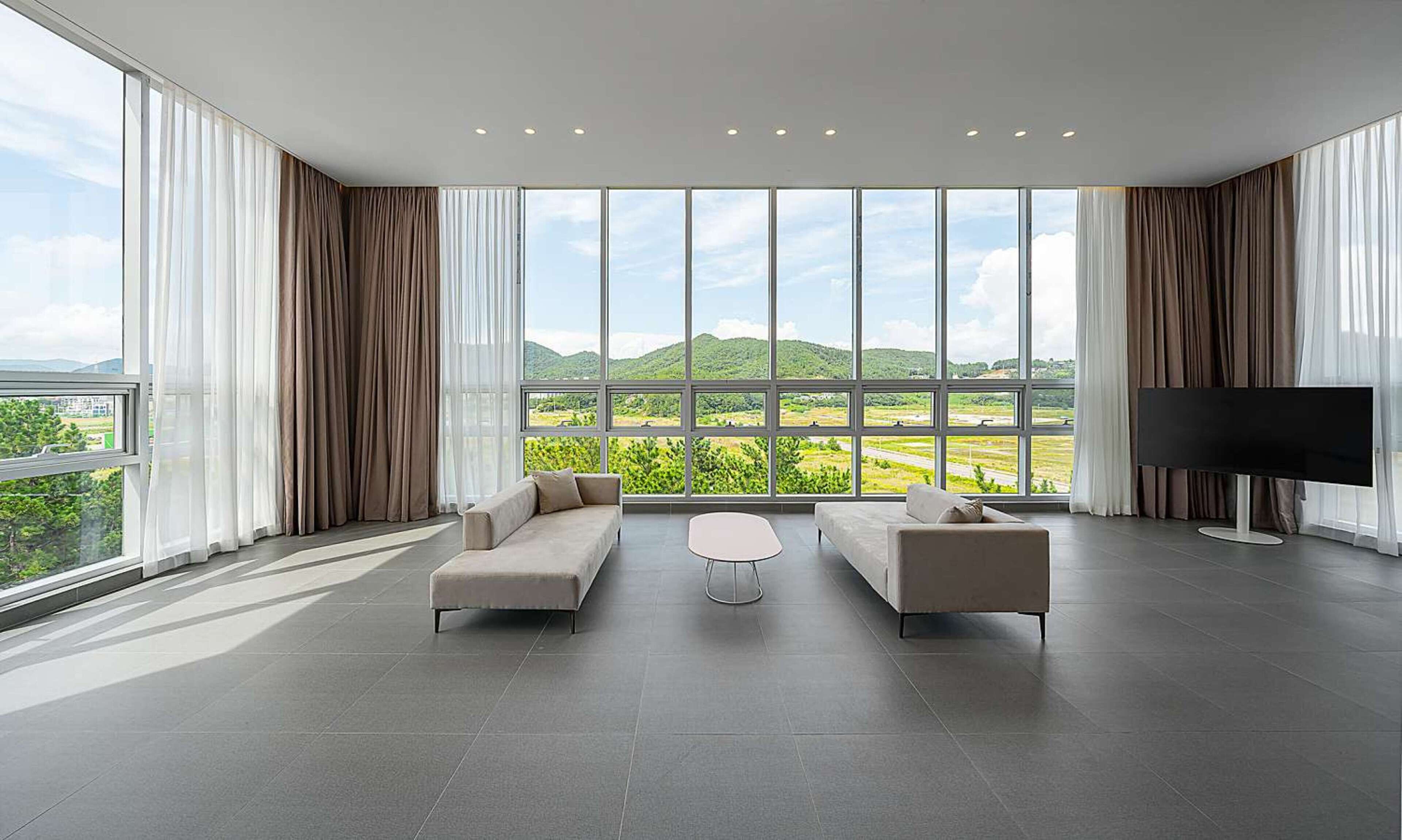 A spacious living room with a large window offering a scenic view of green hills and a clear sky.