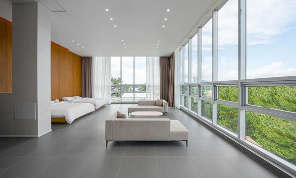 Une chambre d’hôtel moderne, dotée d’un grand lit, d’un canapé et offrant une vue sur la verdure grâce à de grandes fenêtres.