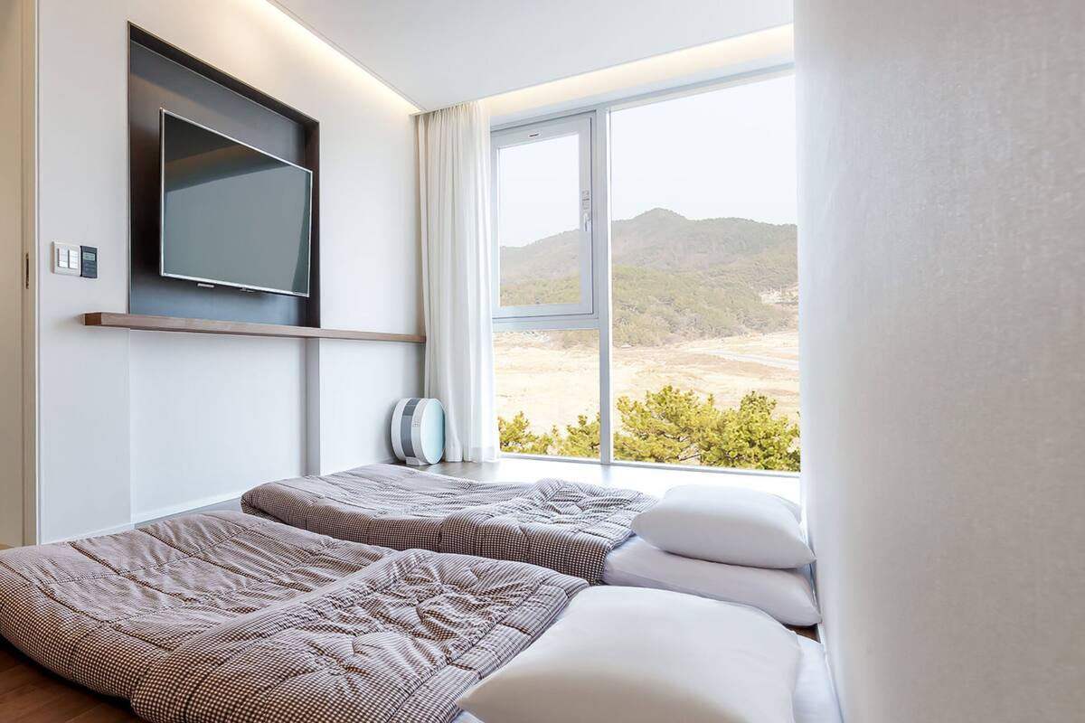 Ein modernes Hotelzimmer mit einem großen Fenster, einem flachbildfernseher an der Wand und zwei Betten mit gemusterten Betttextilien.