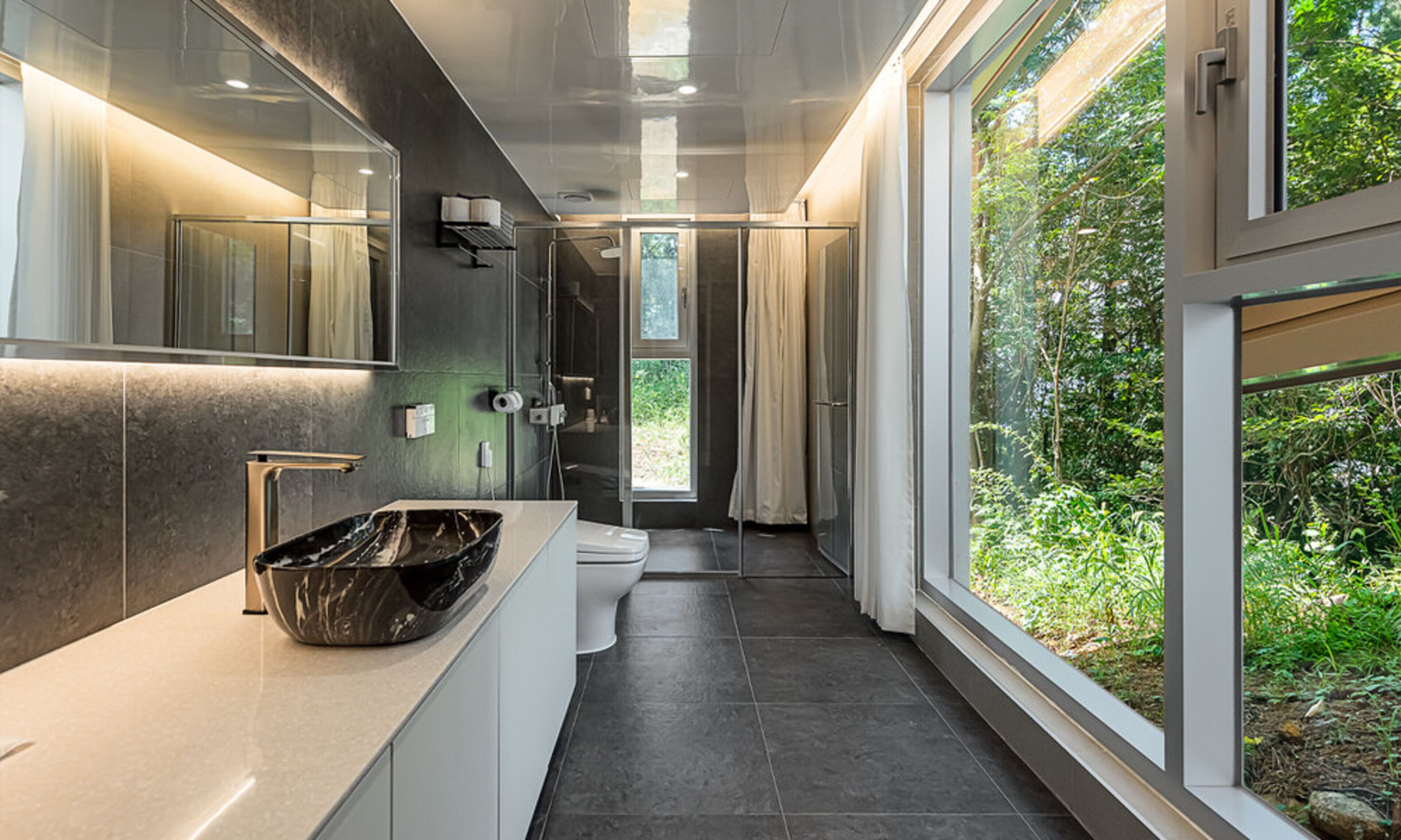 A modern bathroom with a large window, a marble sink, and a toilet.