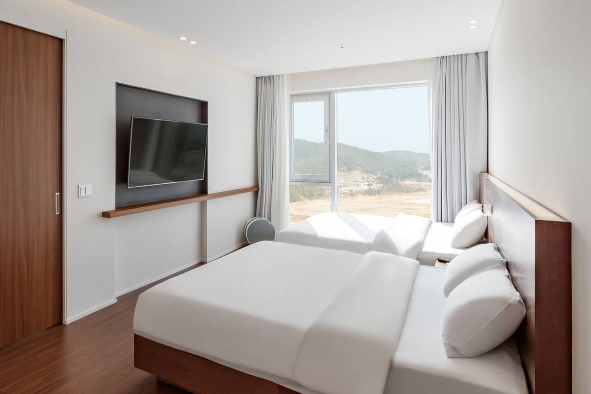 Ein modernes Hotelzimmer mit einem großen Bett, einem flachbildfernseher an der Wand und einem großen Fenster mit Blick ins Freie.
