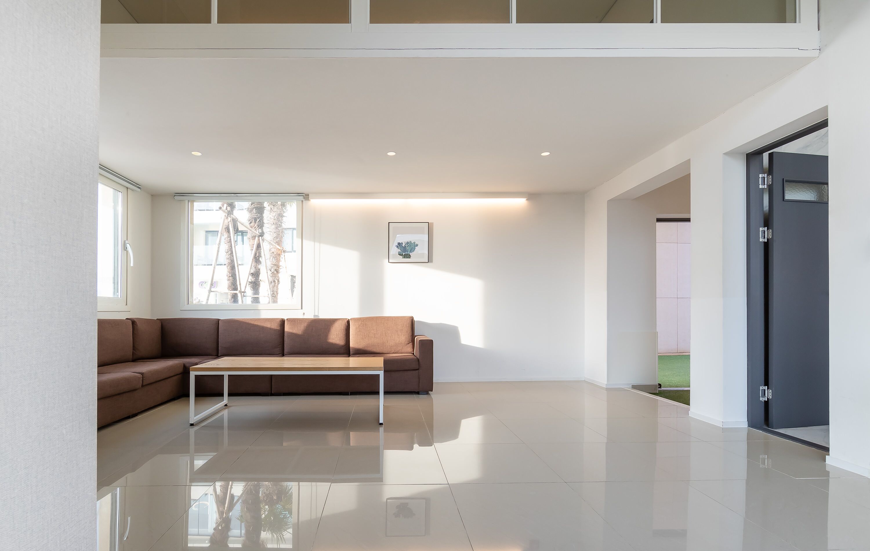 A modern living room with a brown sectional sofa, a coffee table, and a large window providing natural light.