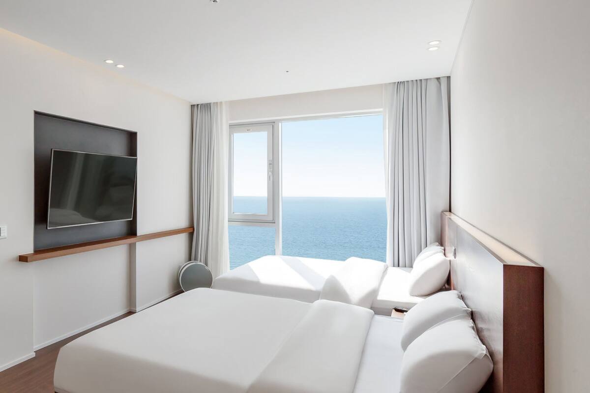 Ein modernes Hotelzimmer mit einem großen Bett, einem flachbildfernseher an der Wand und einem Fenster mit Blick aufs Meer.