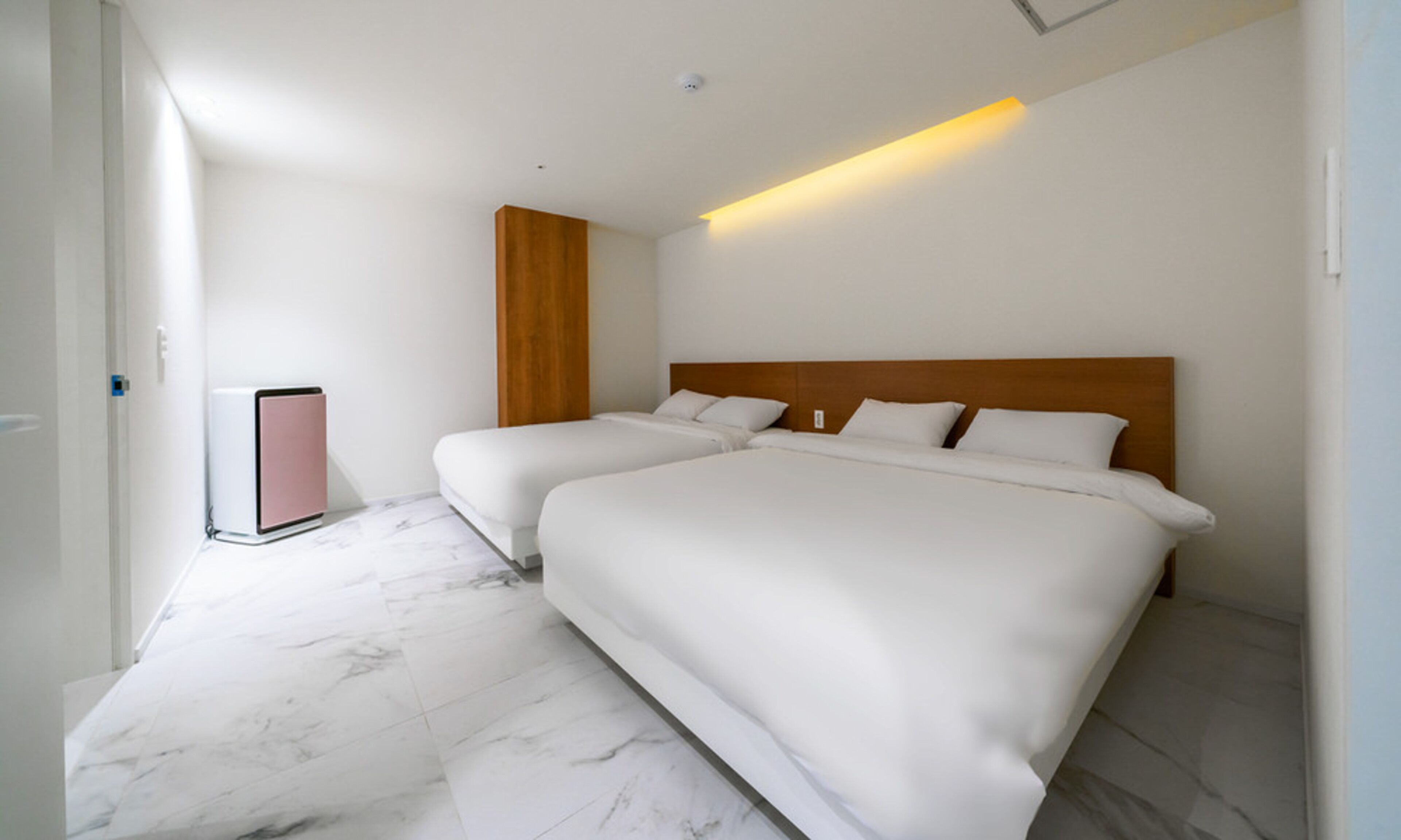 A hotel room with two beds, a wooden headboard, a marble floor, and a wall-mounted heater.