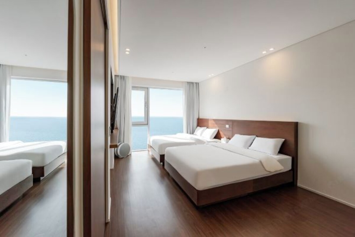 Ein modernes Hotelzimmer mit zwei Betten, einem großen Fenster mit Meerblick und Holzboden.