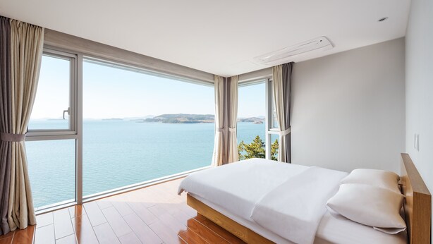 Une chambre avec un grand lit, une vue sur la mer et un plancher en bois.