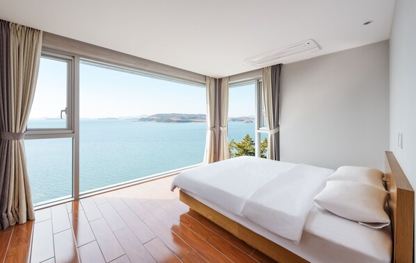A bedroom with a large bed, a view of the sea, and a wooden floor. - La Terrace Resort (Yeosu)