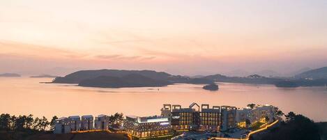 A coastal hotel with modern architecture, a marina, and a view of the sea and distant hills.