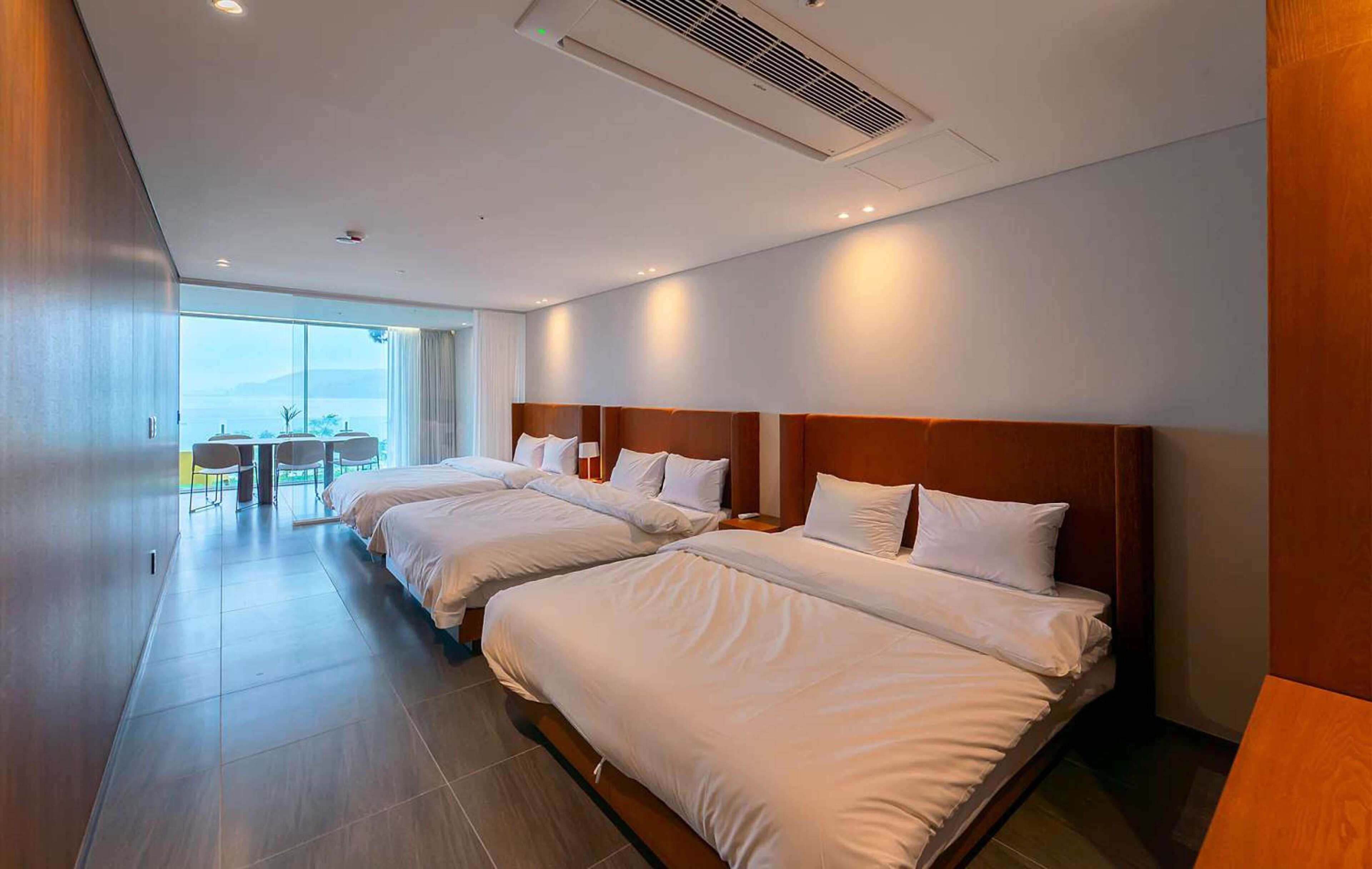 Habitación de hotel con tres camas, un ventanal grande y vistas al exterior.