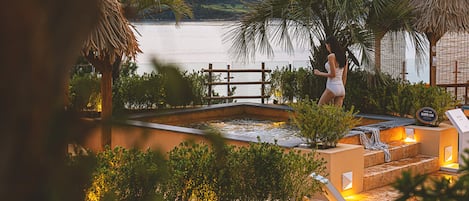Un área de piscina con un jacuzzi, rodeada de plantas tropicales y una valla de madera.