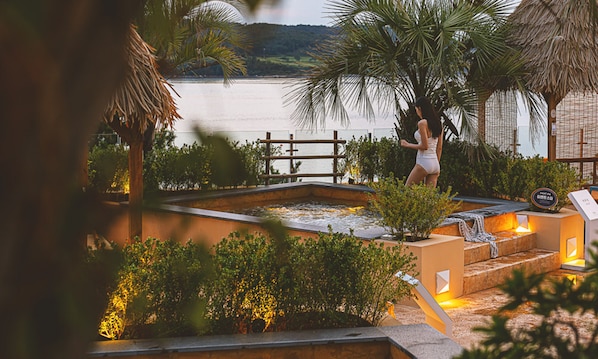 A pool area with a hot tub, surrounded by tropical plants and a wooden fence. - La Terrace Resort (Yeosu)