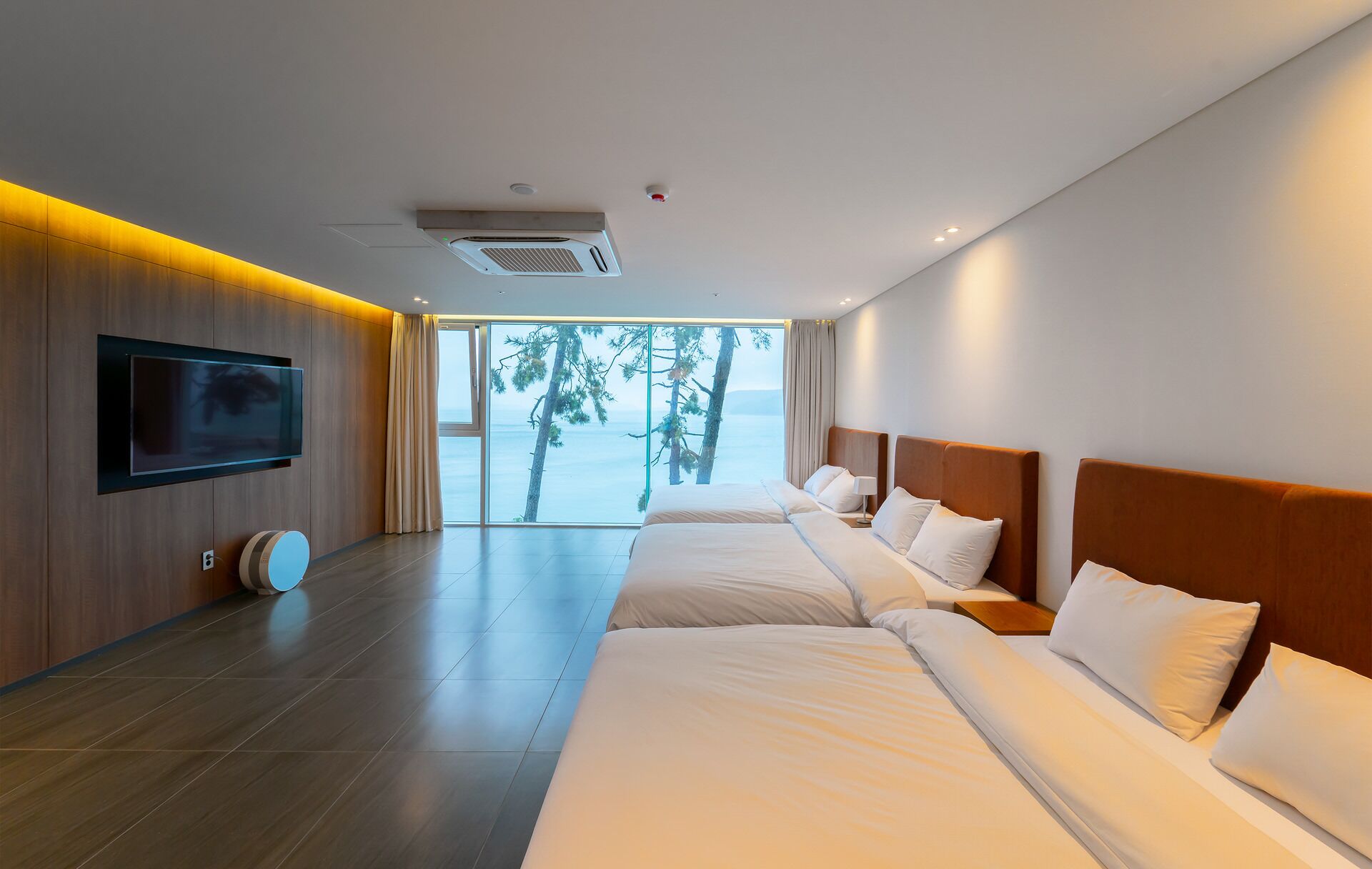 Una habitación de hotel moderna con una cama grande, un televisor de pantalla plana montado en la pared y vista al mar a través de un ventanal amplio.