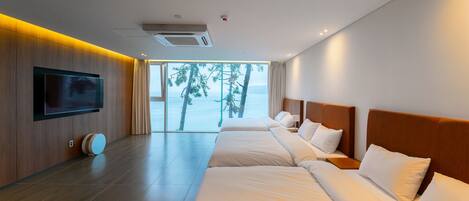 Una habitación de hotel moderna con una cama grande, un televisor de pantalla plana montado en la pared y vista al mar a través de un ventanal amplio.