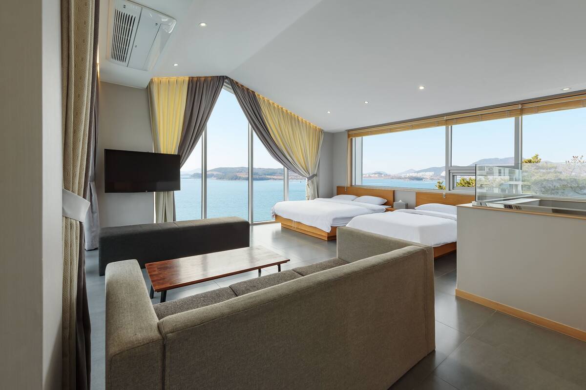 Ein modernes Hotelzimmer mit einem großen Bett, einer Couch, einem Fernseher und Meerblick.