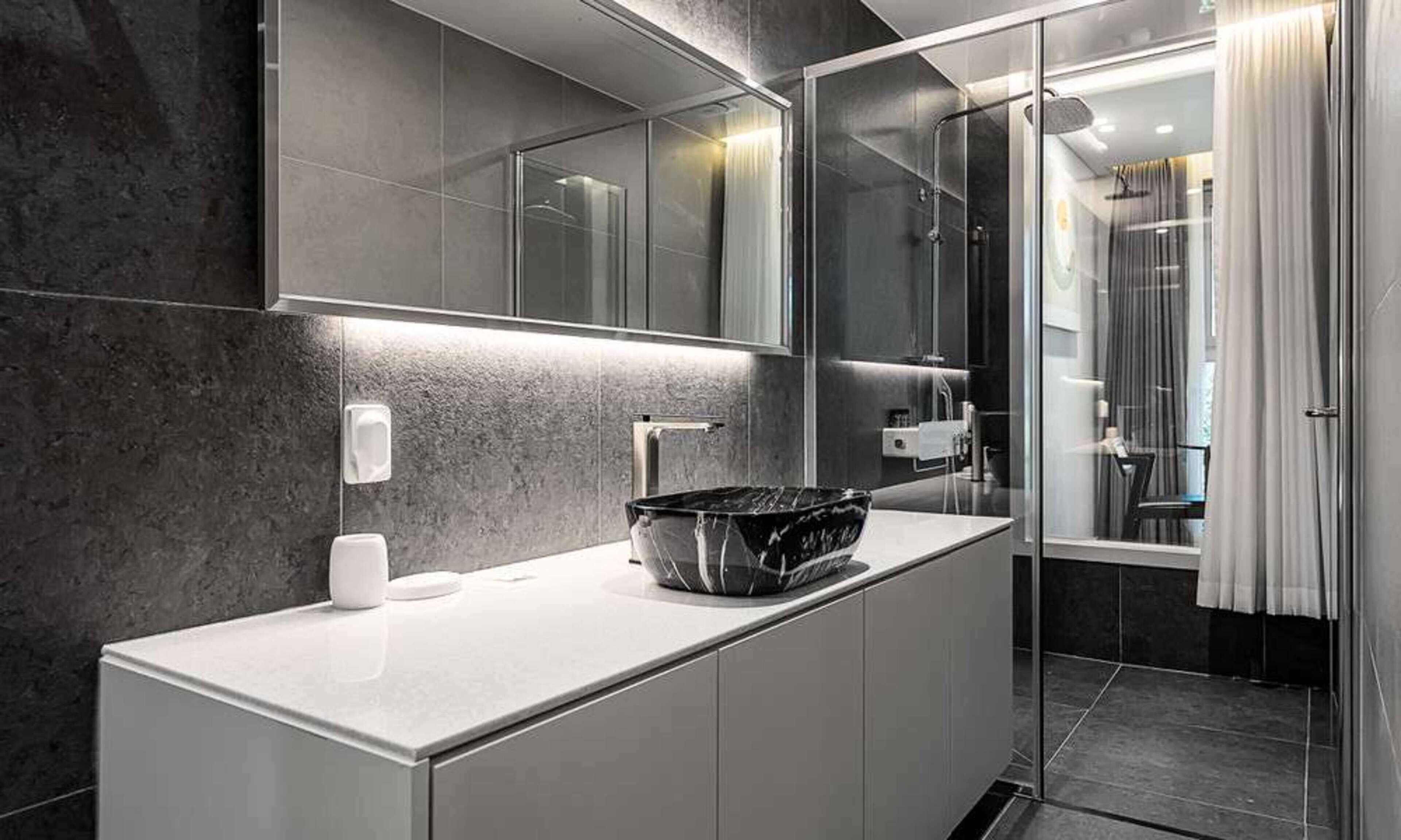 A modern bathroom with a marble countertop, a large mirror, and a glass shower enclosure.