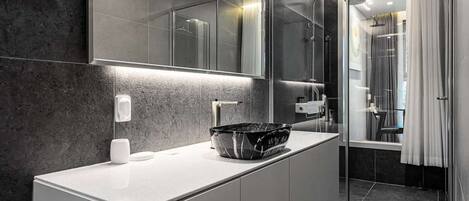 A modern bathroom with a marble countertop, a large mirror, and a glass shower enclosure.