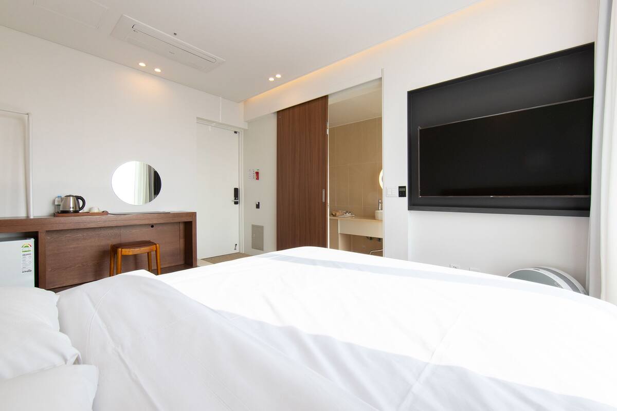 Ein modernes Hotelzimmer mit einem großen Bett, einem Schreibtisch mit Stuhl, einem Spiegel und einem Fernseher.