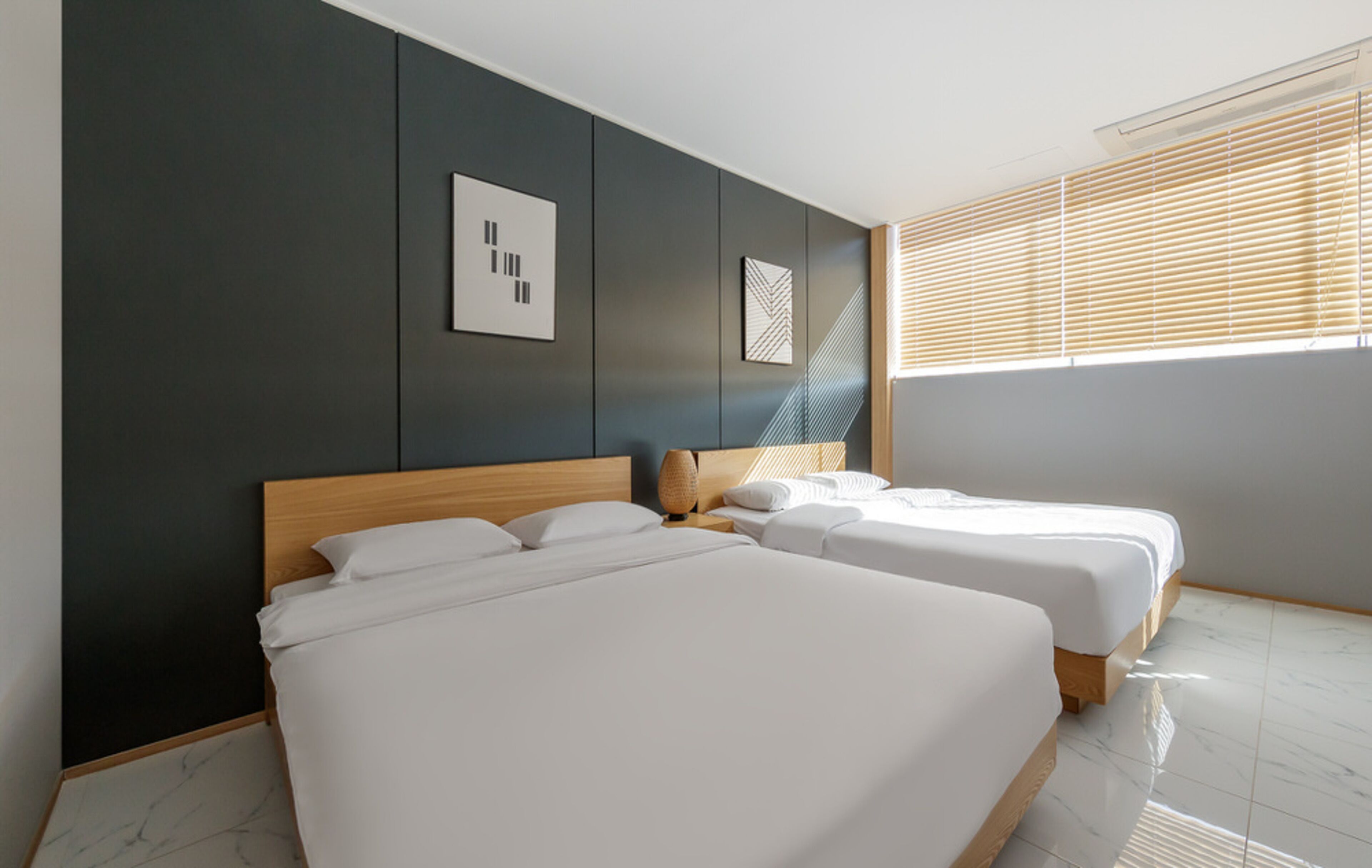 A modern hotel room with two beds, dark walls, and a large window with blinds.