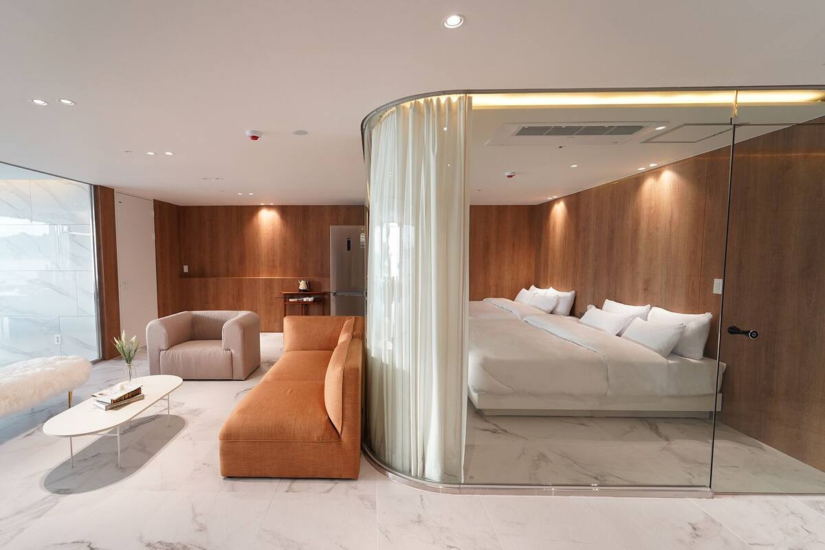 Ein modernes Hotelzimmer mit einer gebogenen Glaswand, einem Sofa, einem Bett und einem Marmorboden.