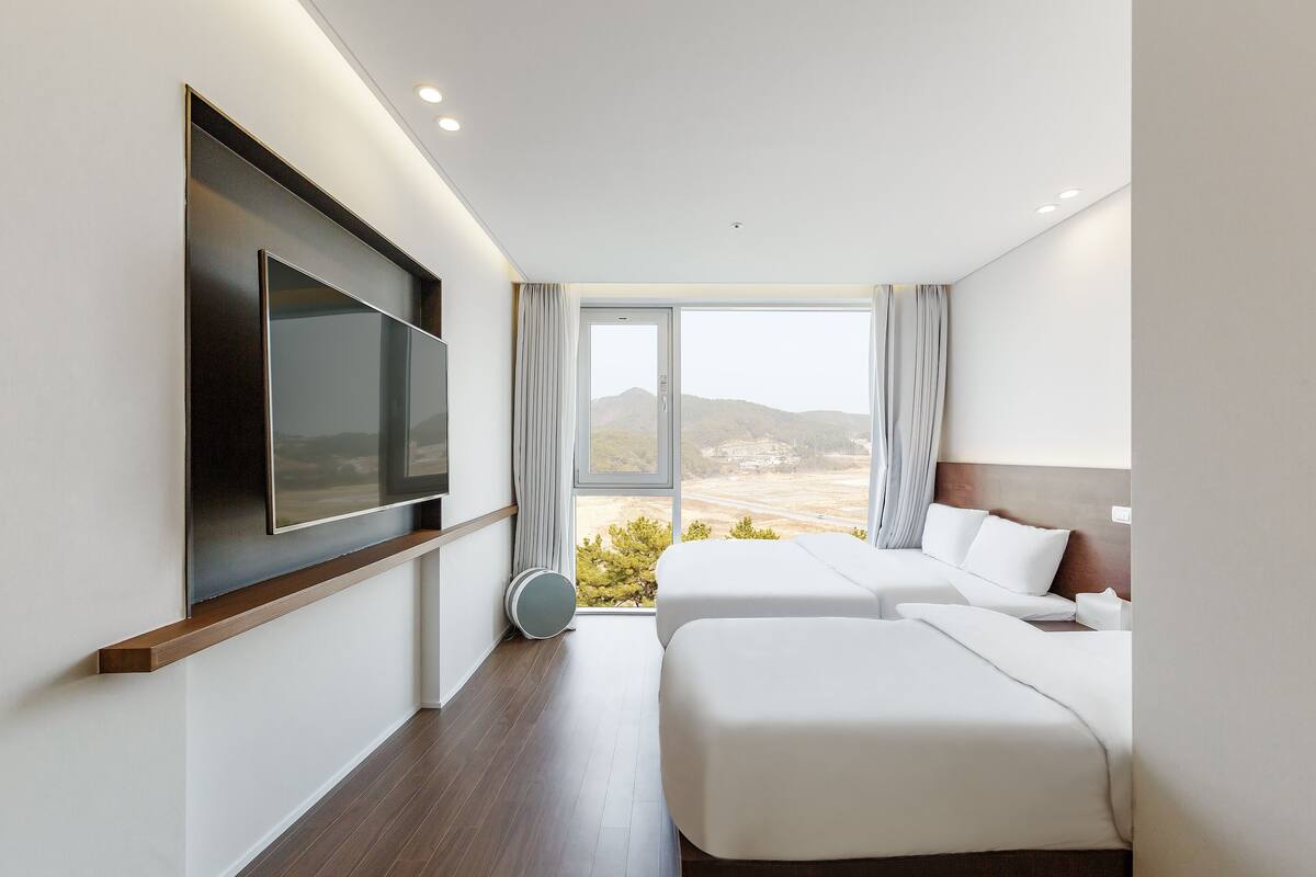 Ein modernes Hotelzimmer mit zwei Betten, einem an der Wand befestigten Flachbildfernseher und einem großen Fenster mit Blick auf die Berge.