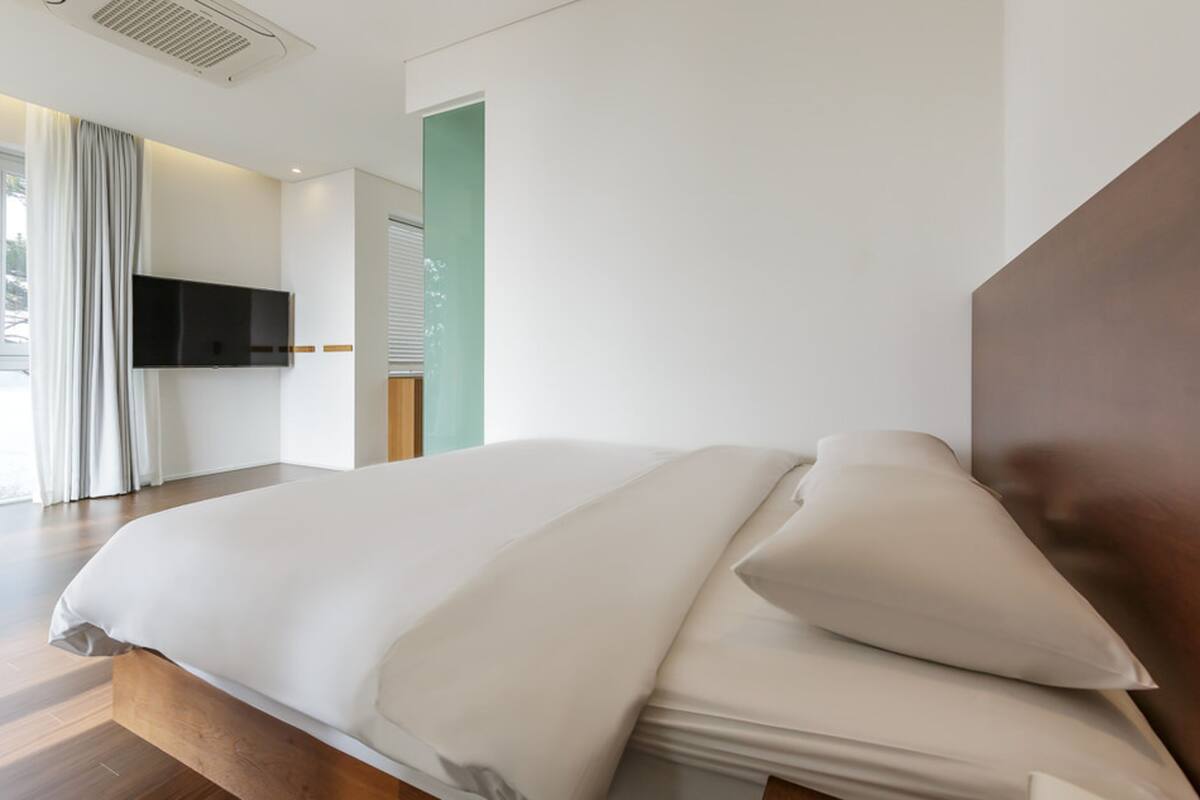 Ein modernes Hotelzimmer mit einem großen Bett, einem flachbildfernseher an der Wand und Blick durch ein Fenster nach draußen.
